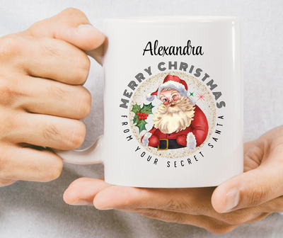 Person holding a mug with a Christmas design featuring Santa Claus and text.
