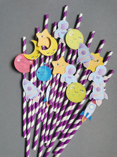 Straw decorations with space-themed designs on purple and white striped straws against a gray background.
