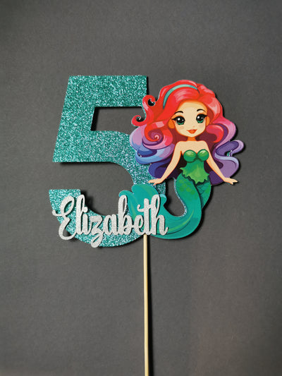 Mermaid-themed with number cake topper with glittery teal color on a gray background