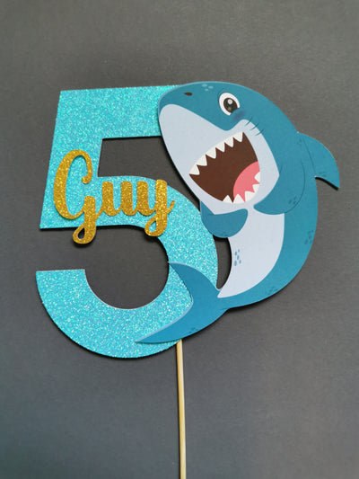 Shark-themed number cake topper with name on a gray background
