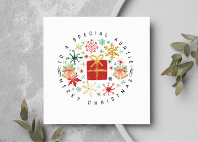 Christmas card with decorative wreath and text on a gray surface with greenery.