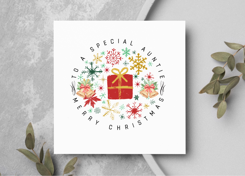 Christmas card with decorative wreath and text on a gray surface with greenery.