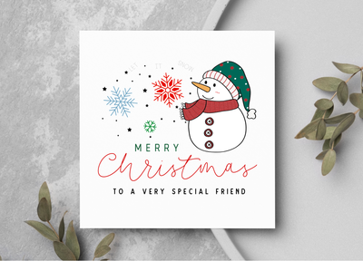 Christmas card with a snowman and festive text on a gray surface with greenery.