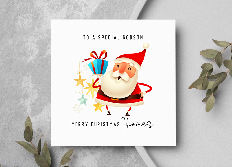 Christmas card with Santa Claus holding gifts on a gray surface with greenery.