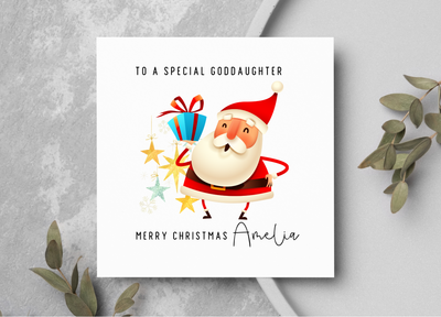 Christmas card with Santa Claus holding presents on a gray surface with greenery.
