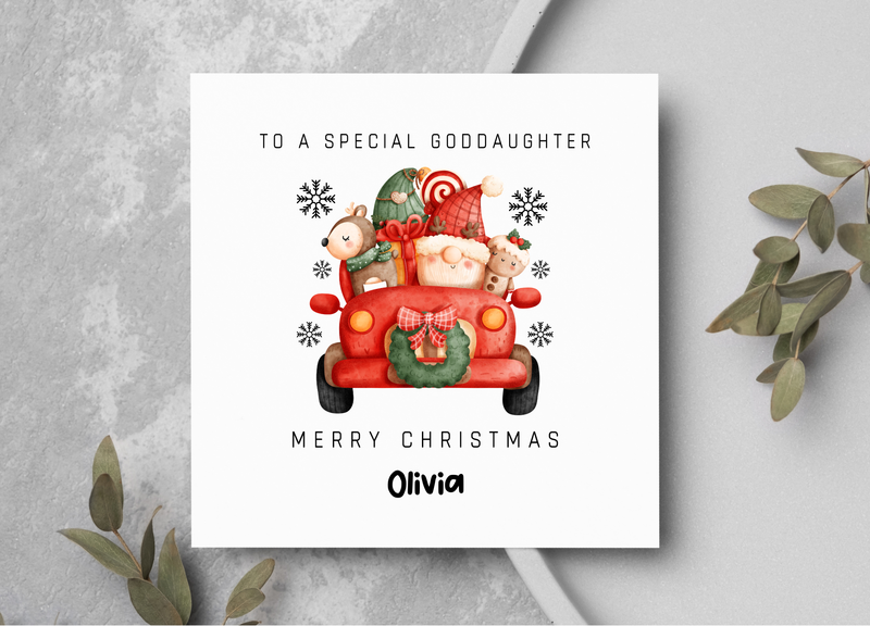 Christmas card with a red truck and teddy bears on a gray surface with greenery.