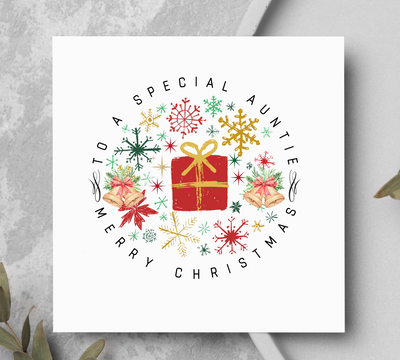 Christmas card with decorative wreath and text on a gray surface with greenery.