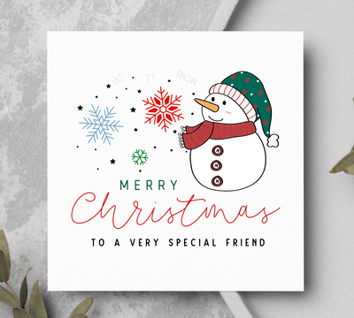 Christmas card with a snowman and festive text on a gray surface with greenery.