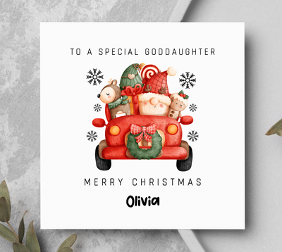 Christmas card with a red truck and teddy bears on a gray surface with greenery.