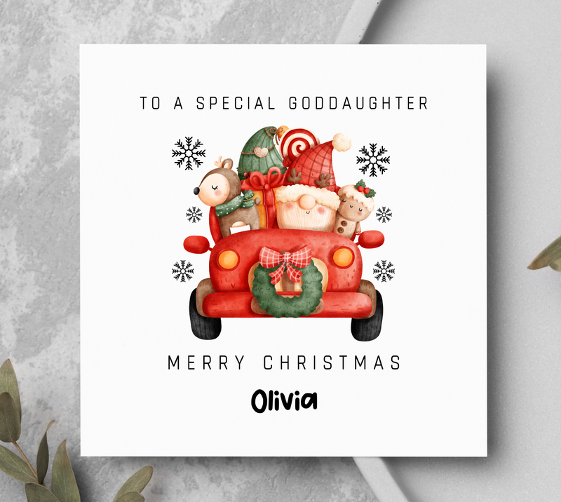 Christmas card with a red truck and teddy bears on a gray surface with greenery.